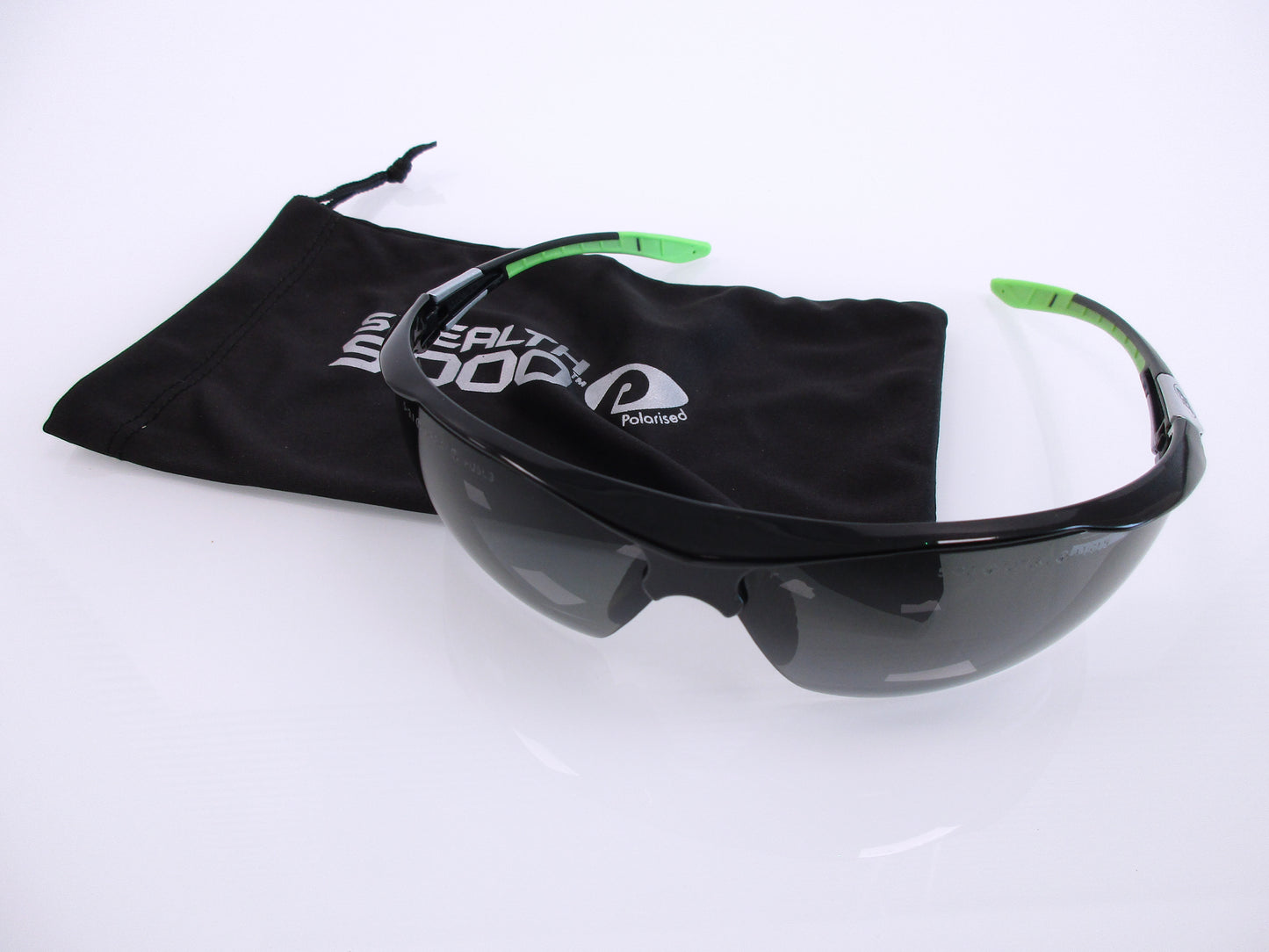 Black shield-style safety glasses with dark lenses, and bright green temple tips, displayed with a black drawstring pouch printed with the White Spot brand logo on a white background.