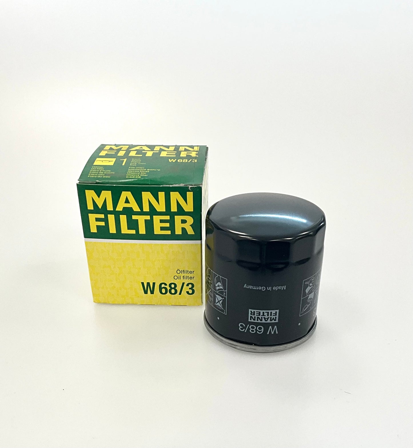 A black Mann Filter W68/3 oil filter next to its original green and yellow packaging box, on a white studio background.