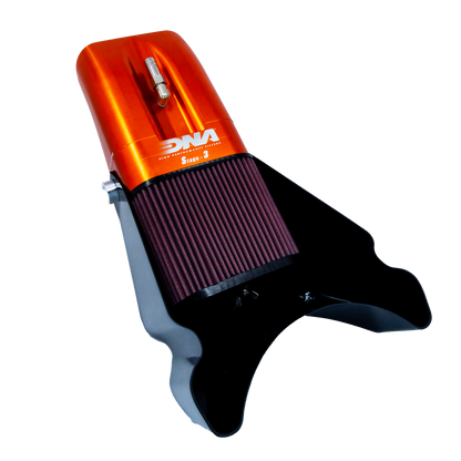 An motorcycle air filter assembly or air box, featuring a metallic orange top section with a grey metal valve and white 'DNA' branding, a dark red pleated filter element, and a black mounting base, shown on a white background.