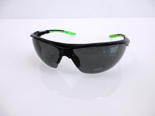 Black shield-style safety glasses with dark lenses and bright green temple tips, photographed on a clean white studio surface.