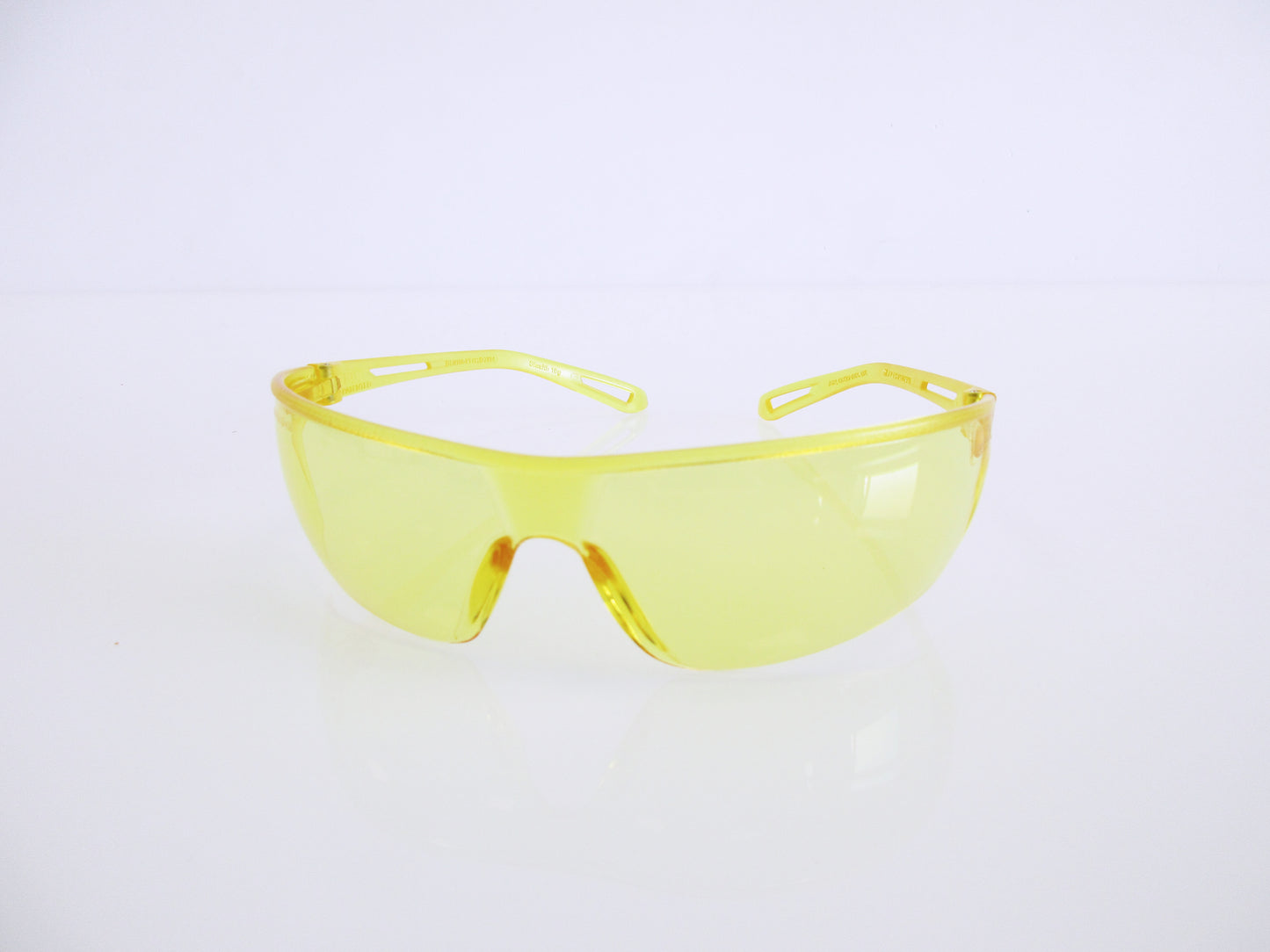 Yellow safety glasses with a translucent yellow frame and yellow-tinted lenses, displayed on a clean white reflective surface.