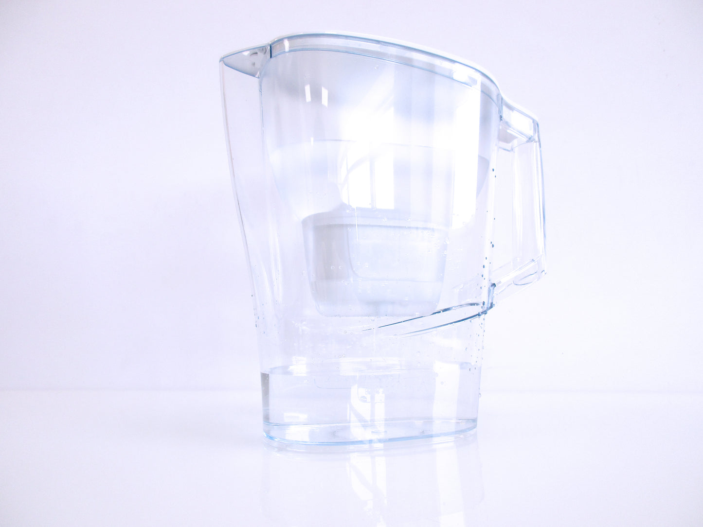 A clear plastic water filter jug, with a handle and spout, shown on a clean white background with a soft reflection below.