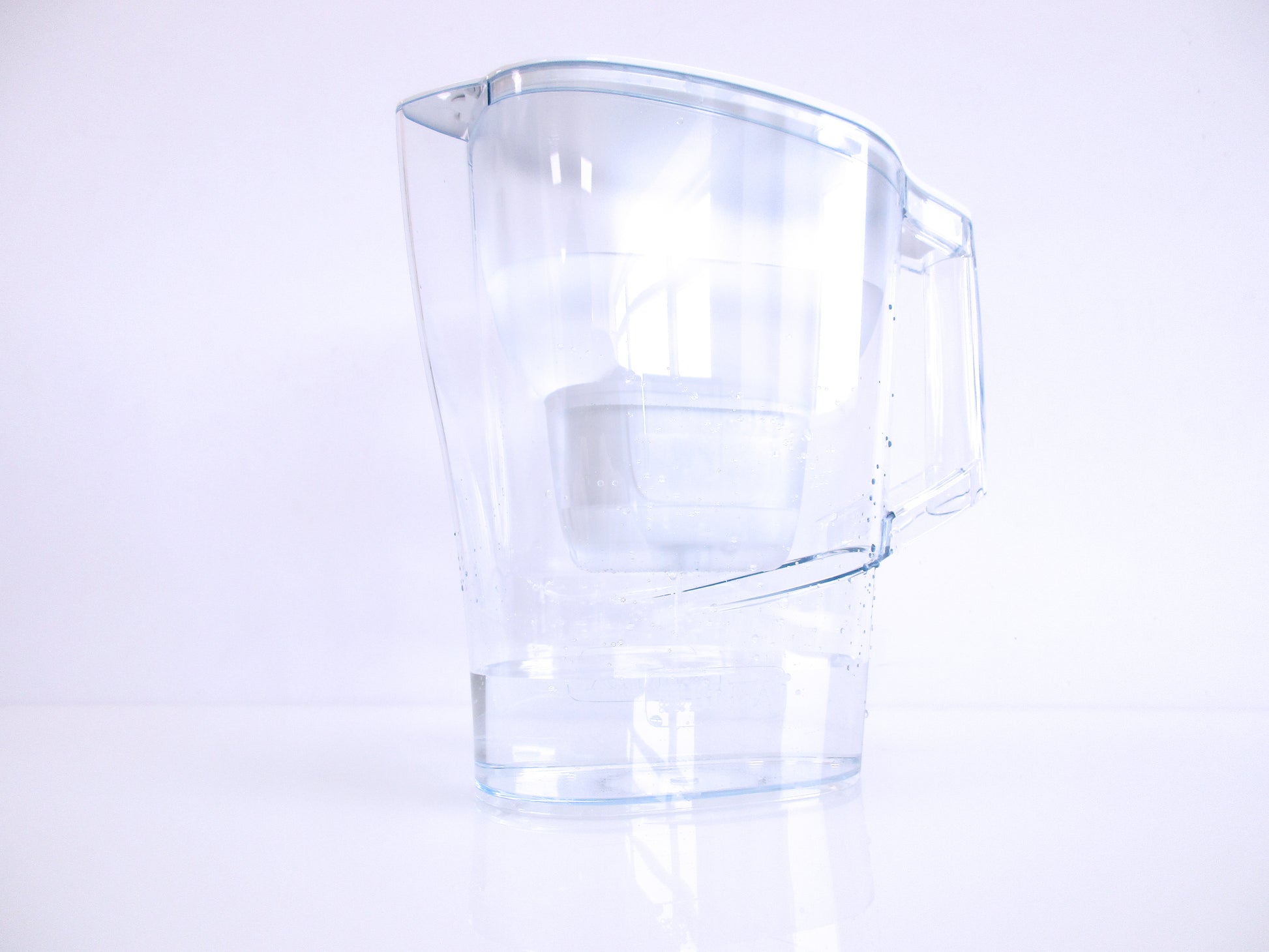 A clear plastic water filter jug, with a handle and spout, shown on a clean white background with a soft reflection below.