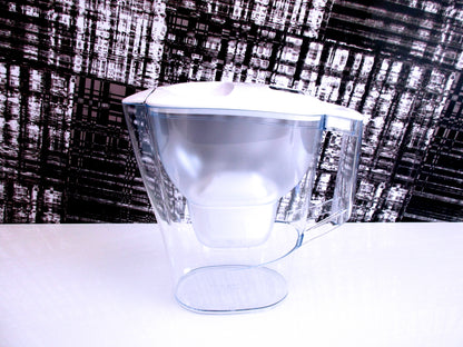 A clear plastic water filter jug with a white lid, shown on a white surface against a black and white textured background.
