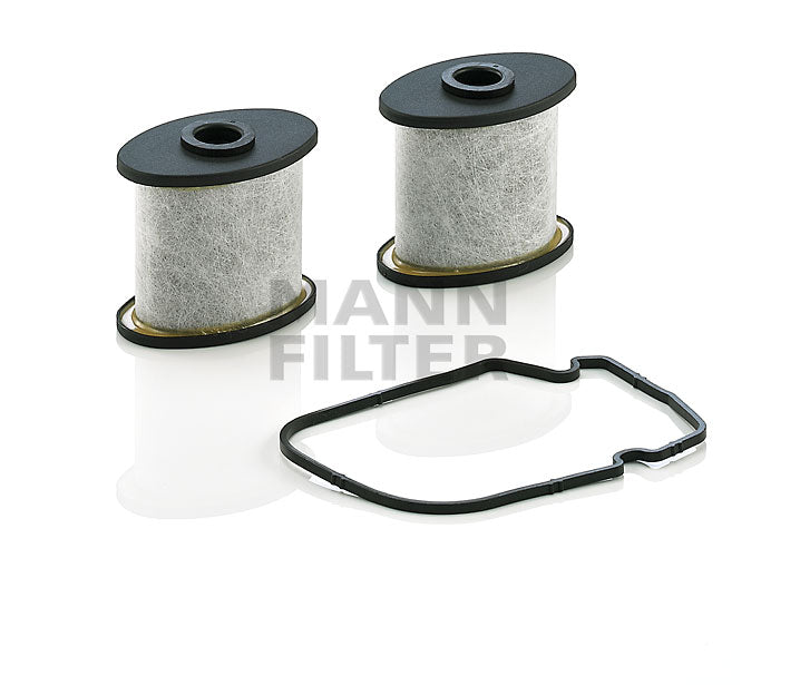 Two cylindrical ventilators, with black tops and bottoms, shown alongside a black rubber gasket on a white reflective background. A semi-transparent 'MANN FILTER' logo watermark is visible in the centre.