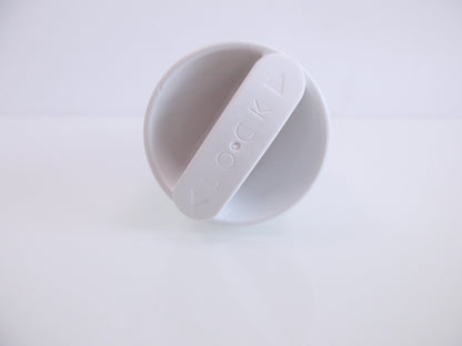 A white plastic circular cap for FTL3957, with a diagonal tab embossed with the word 'LOCK', photographed on a seamless white background.
