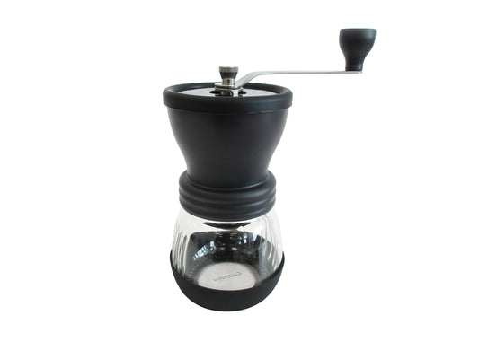 A manual coffee grinder with a matte black body, a clear glass carafe, and a silver metal hand crank, shown against a plain white background.
