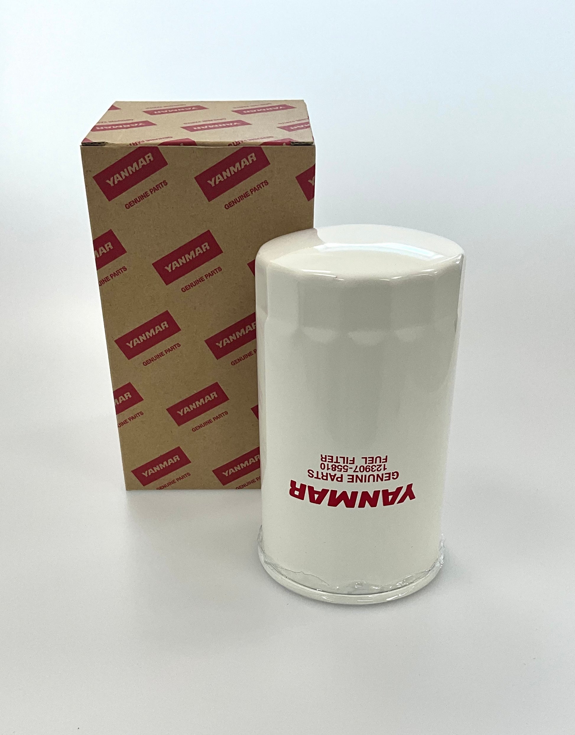 A white cylindrical genuine Yanmar fuel filter standing next to its brown cardboard packaging box with red printed Yanmar logos, on a clean white background.