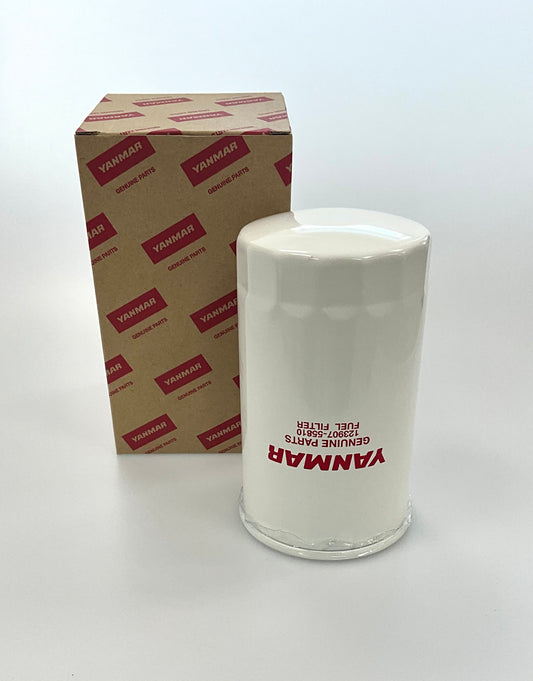 A white cylindrical genuine Yanmar fuel filter standing next to its brown cardboard packaging box with red printed Yanmar logos, on a clean white background.