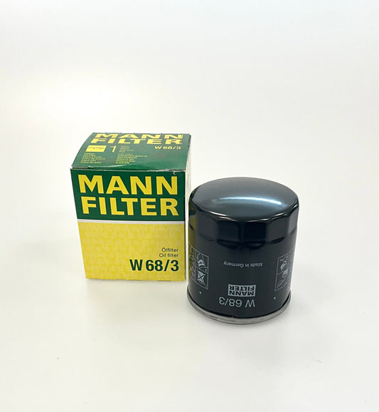 A black Mann Filter W68/3 oil filter next to its original green and yellow packaging box, on a white studio background.